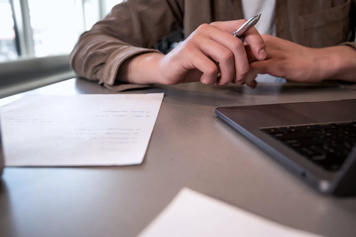 Des mains prennent des notes à côté d'un ordinateur portable